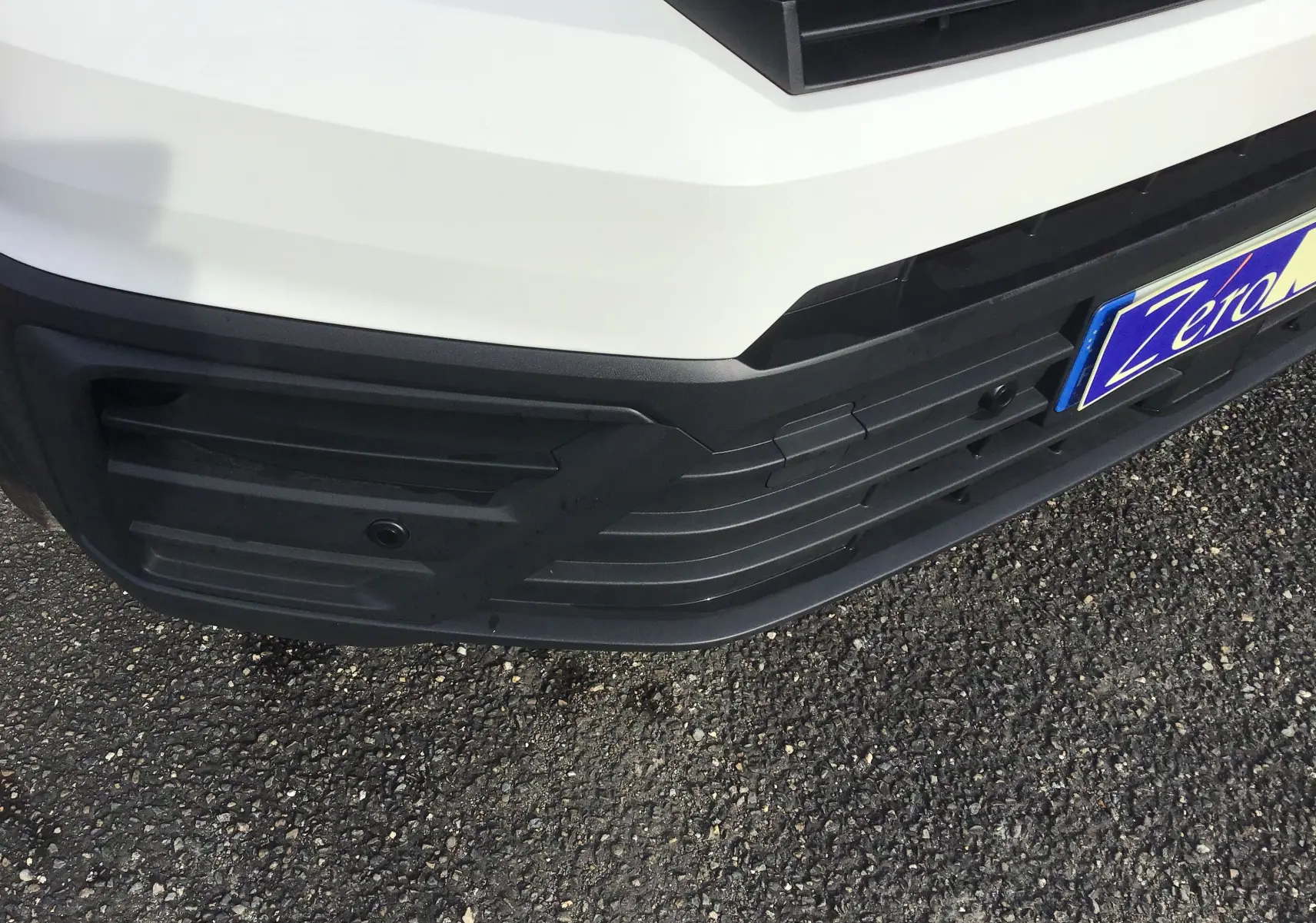 Gros plan sur le pare-chocs avant blanc du Volkswagen Crafter Fourgon 2024 avec caméra de recul intégrée.