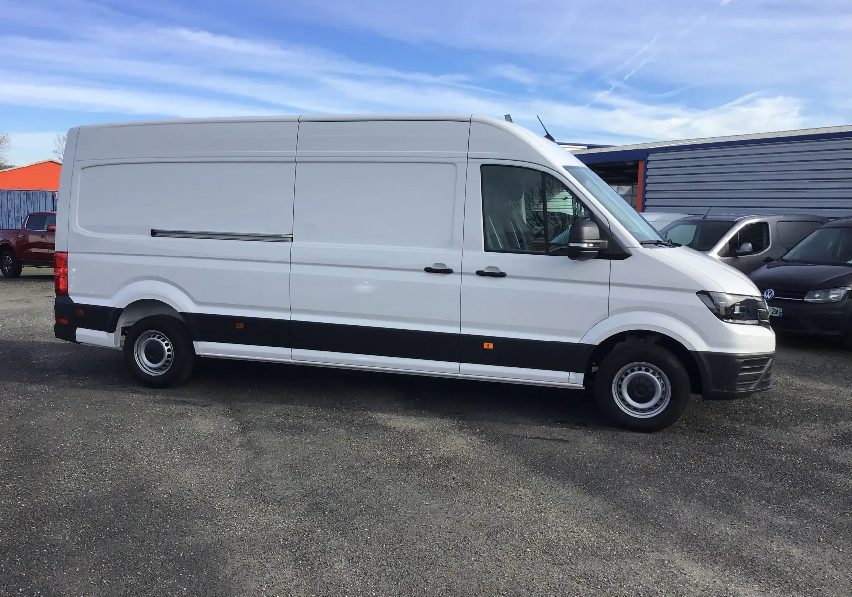 Volkswagen Crafter blanc vu de profil côté gauche, fourgon utilitaire long avec bande noire basse et jantes acier.