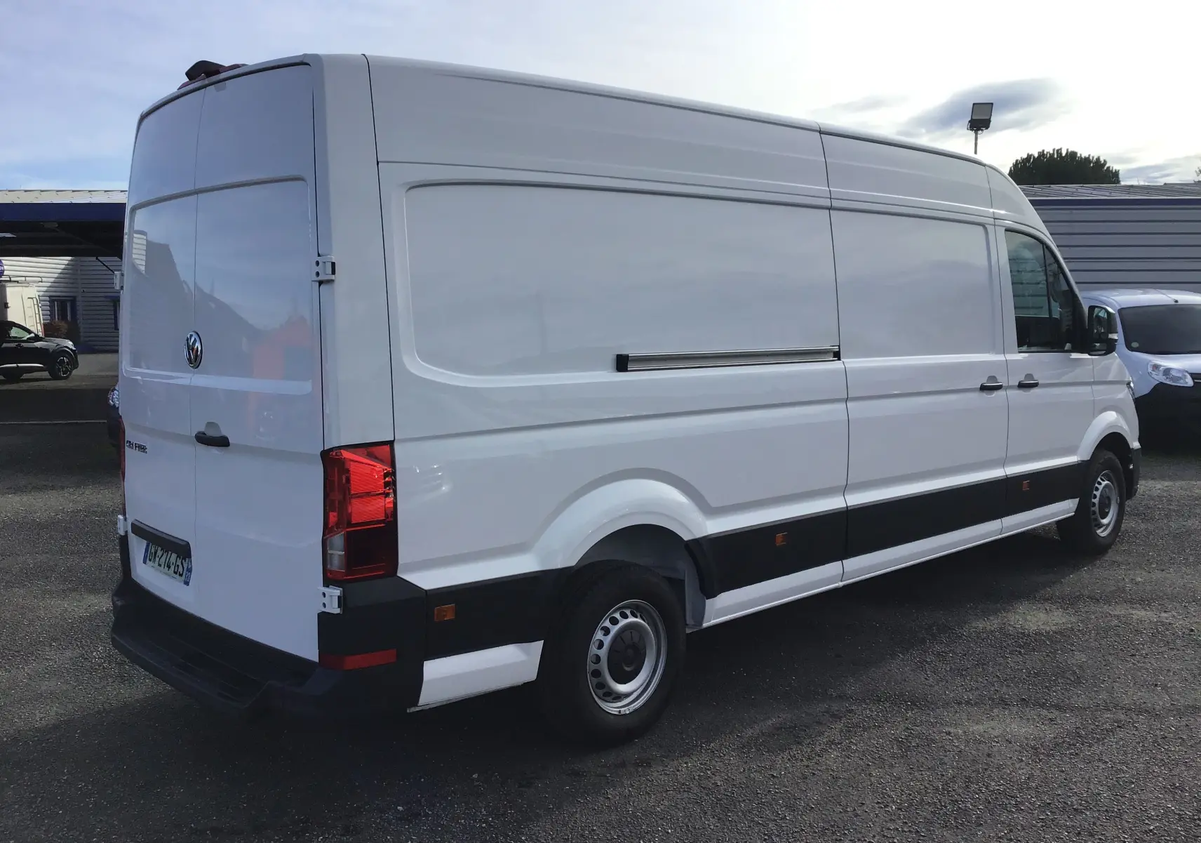 Volkswagen Crafter fourgon blanc en vue 3/4 arrière droit, soulignant sa grande taille et ses feux arrière rouges.