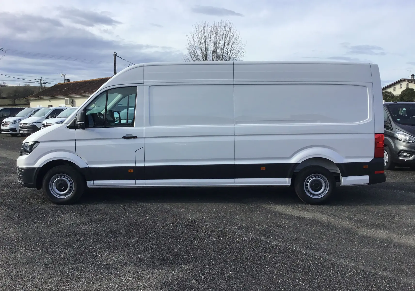 Profil côté gauche d'un utilitaire Volkswagen Crafter blanc 2024, version L4H3, avec bande noire basse et roues acier.
