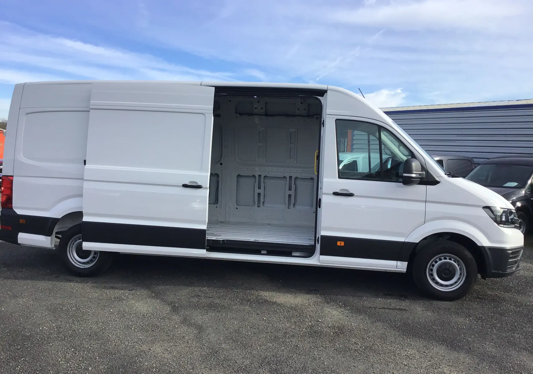Vue latérale droite d'un Volkswagen Crafter blanc 2024 avec porte coulissante ouverte dévoilant l'espace de chargement vide.
