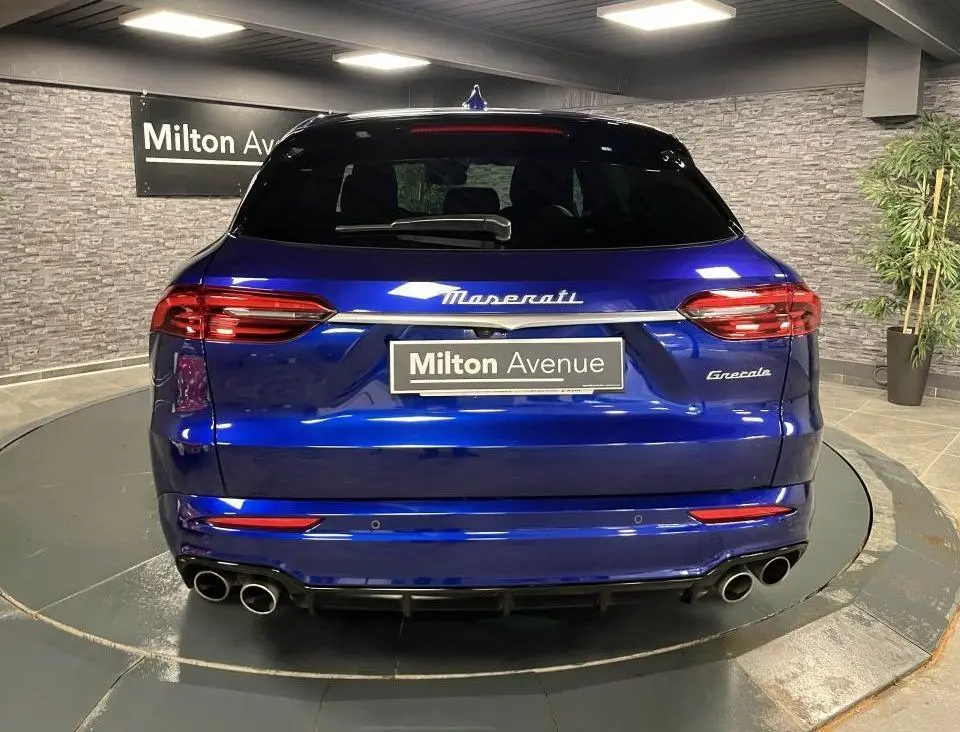 Vue arrière d'une Maserati Grecale bleu brillant avec quadruple sortie d'échappement et logo Maserati lumineux.