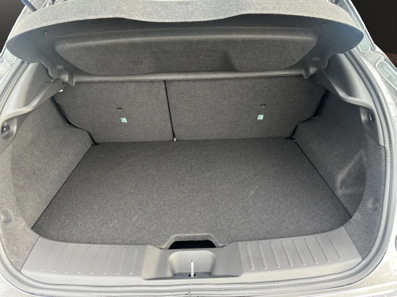 Coffre spacieux et propre du Nissan Juke Full Hybrid 2025, vu de l'arrière avec intérieur gris foncé.