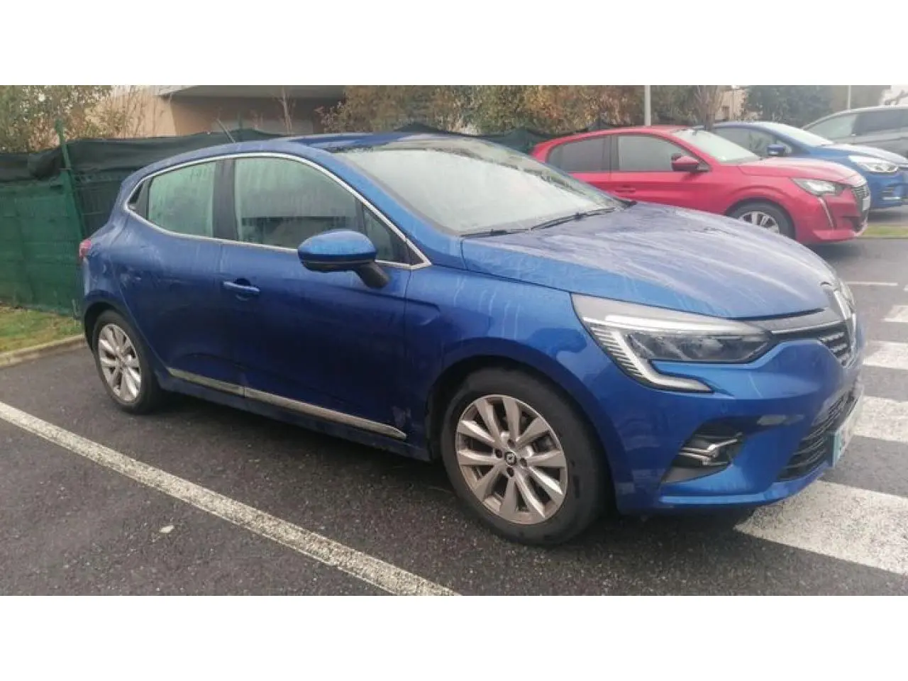 Renault Clio Bleu Iron vue de profil gauche, garée sur un parking avec jantes alliage et feux LED distinctifs.