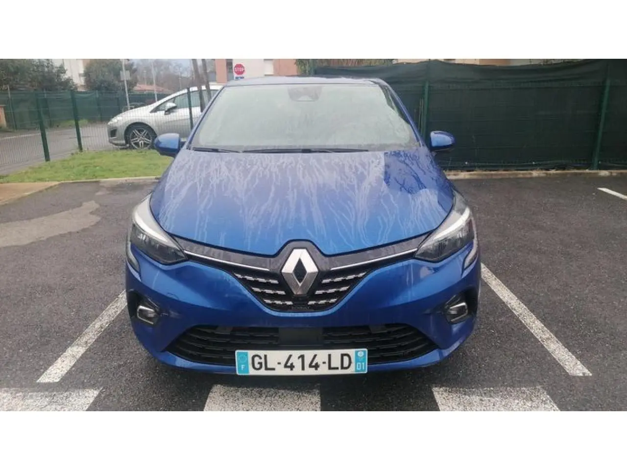 Vue avant d'une Renault Clio 2021 bleu Iron avec calandre chromée et phares LED allumés sur parking.