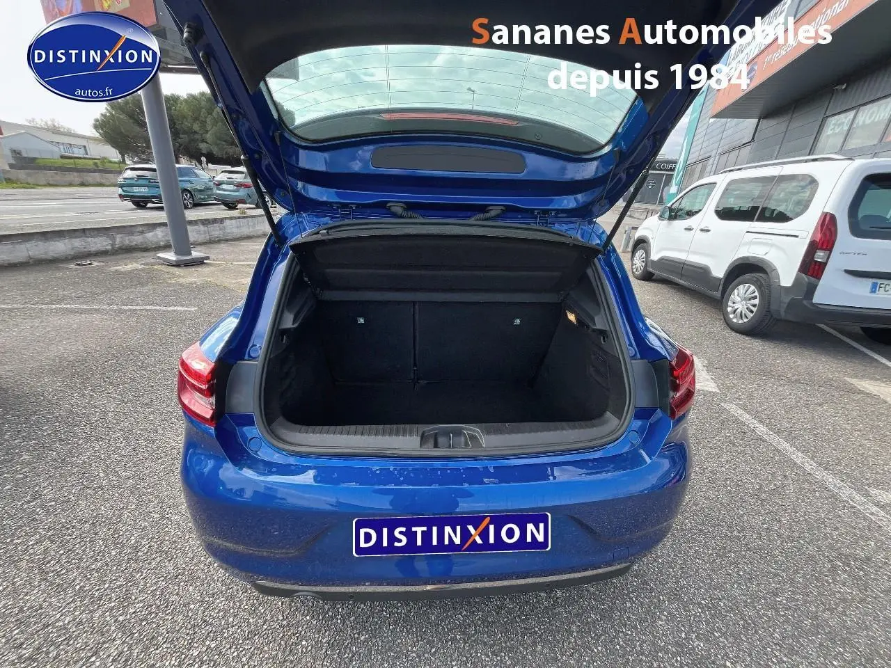 Vue arrière de la Renault Clio 1.0 Tce Intens 2021 en Bleu Iron avec coffre ouvert sur parking extérieur.