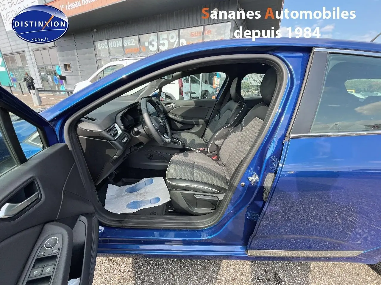 Vue latérale gauche sur l'intérieur d'une Renault Clio Bleu Iron 2021, avec sièges en velours et cuir synthétique noir.