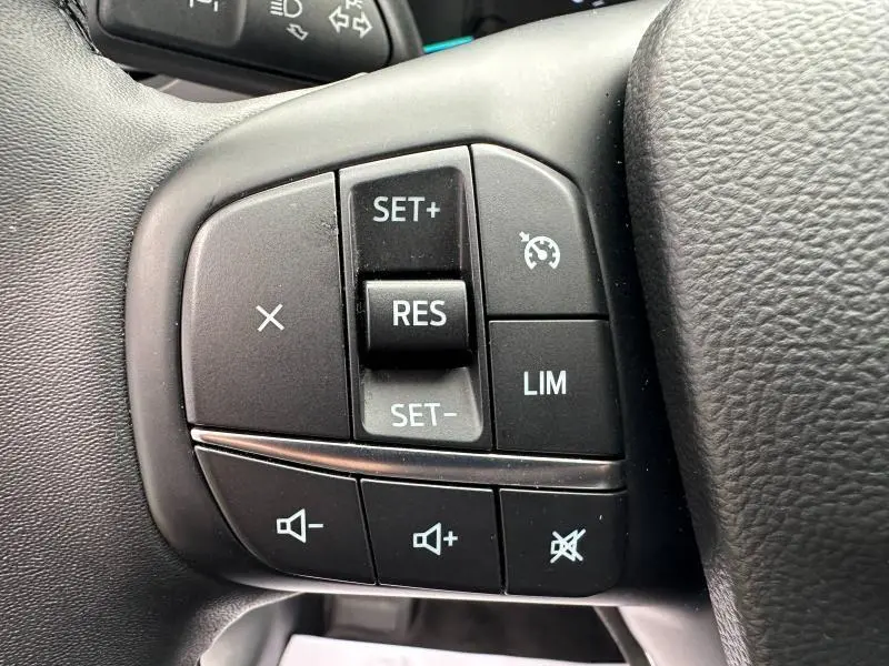 Gros plan sur les commandes du volant cuir noir du Ford Kuga 2024, boutons de régulateur de vitesse et volume sonore.