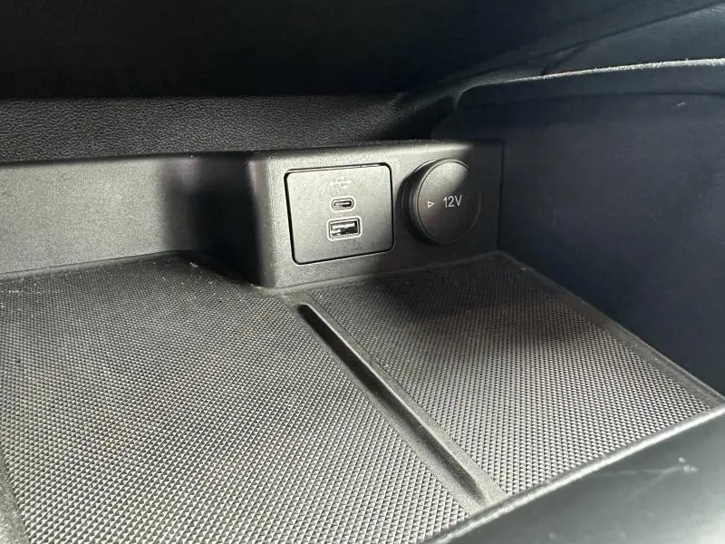 Gros plan sur la prise USB et prise 12V dans l'accoudoir central noir du Ford Kuga 2024.