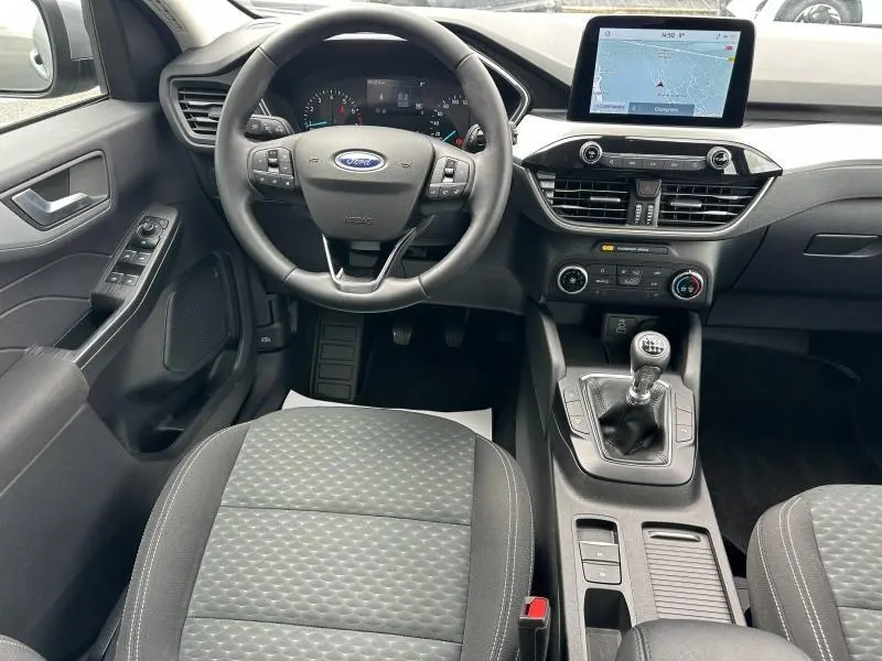 Vue intérieure avant du Ford Kuga 2024 avec volant cuir multifonction, écran tactile GPS et levier de vitesse manuel.