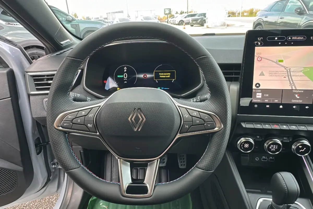 Vue intérieure centrée sur le volant cuir multifonctions de la Renault Clio gris rafale avec tableau de bord digital et écran tactile.