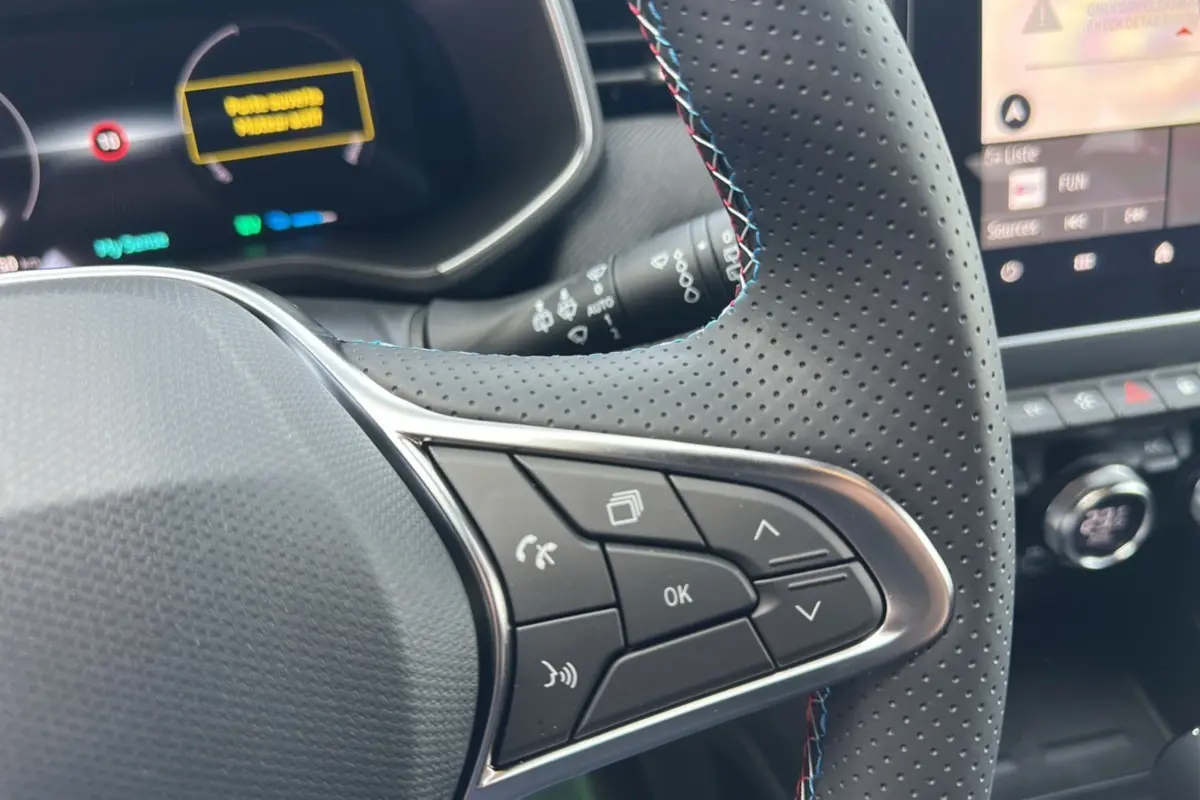 Gros plan sur le volant cuir perforé de la Renault Clio V E-Tech 145 Esprit Alpine Bose avec commandes multifonctions.