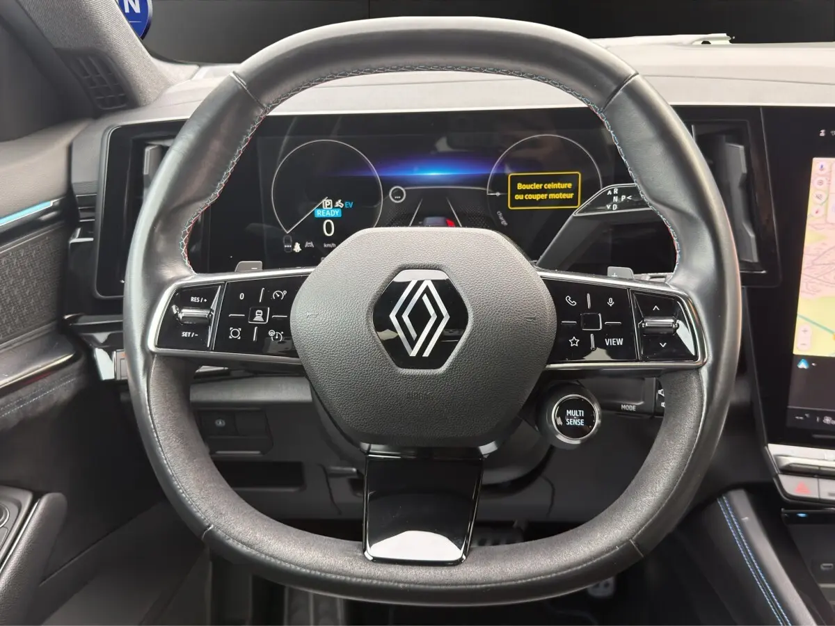 Vue frontale du volant cuir noir avec logo Renault, tableau de bord numérique et écran tactile latéral du Renault Austral gris foncé.