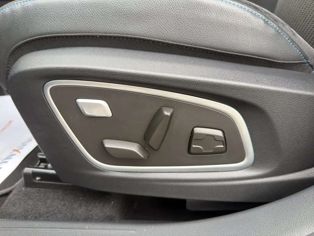 Gros plan sur les commandes de réglage électrique du siège en cuir noir avec surpiqûres bleues du Renault Austral gris foncé.