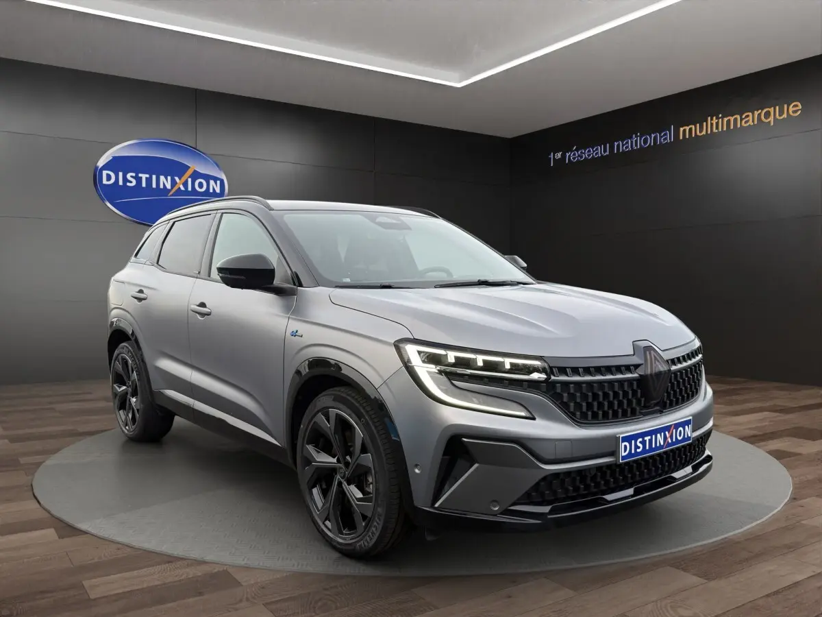 Renault Austral gris foncé en 3/4 avant droit, avec calandre noire et phares LED distinctifs allumés.