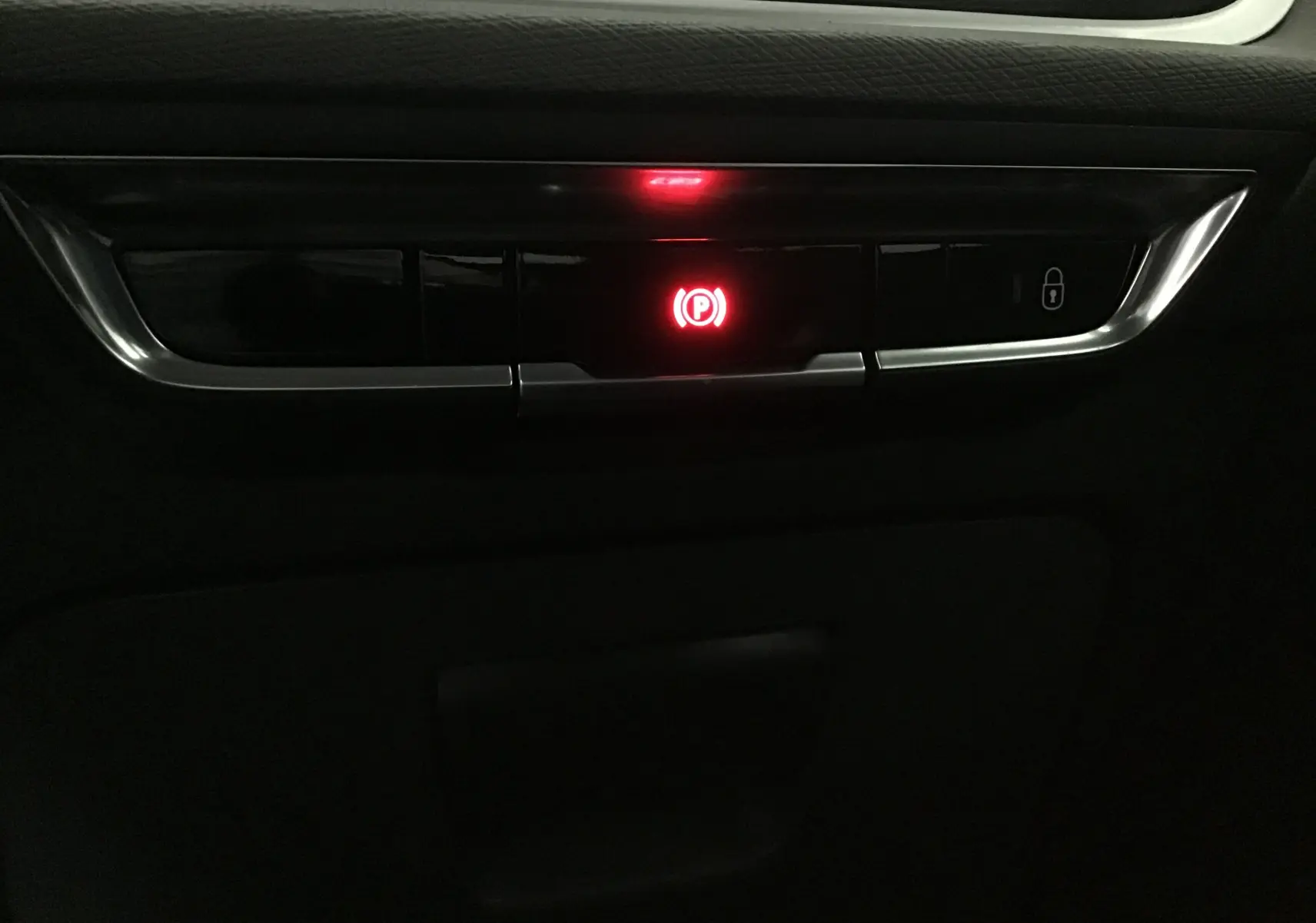 Gros plan sur le bouton de frein à main électrique rouge dans l'habitacle noir du Citroën Grand C4 Spacetourer gris Artense.