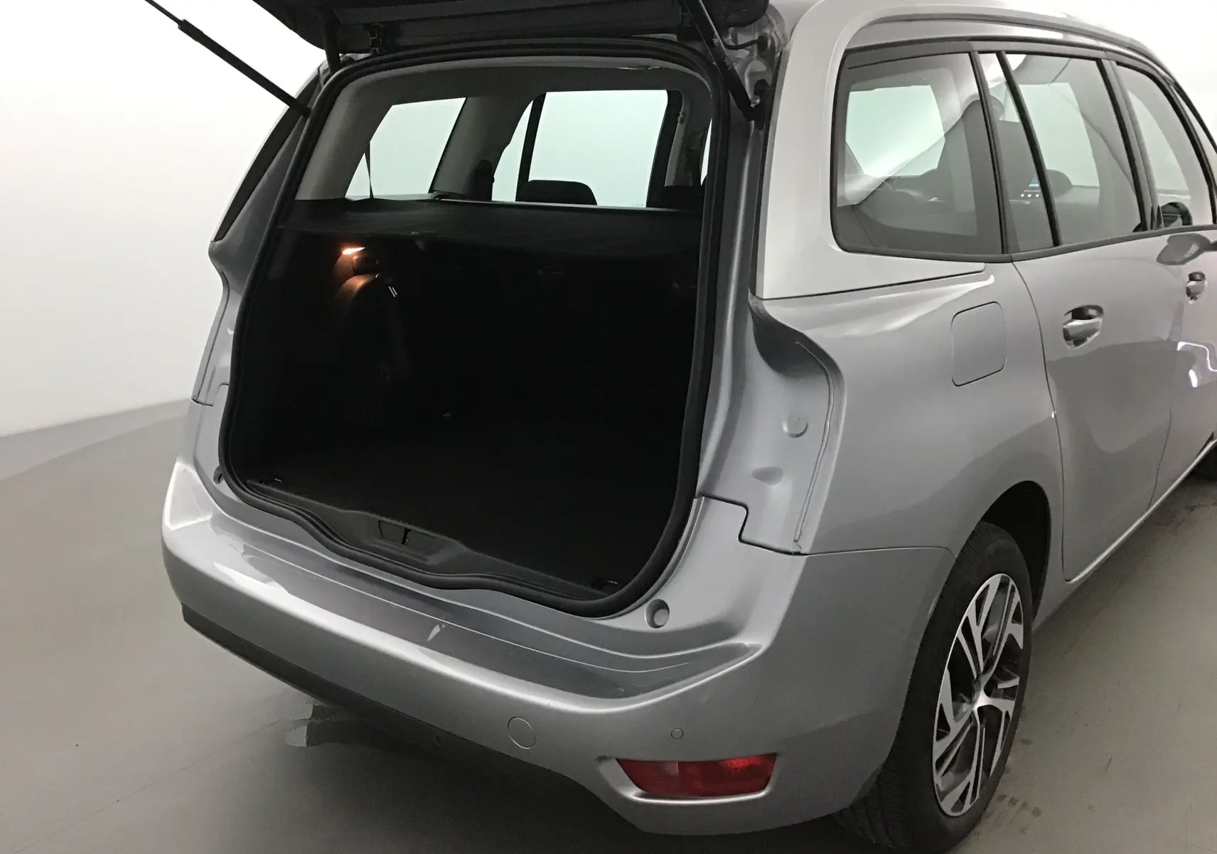Vue arrière côté droit d'un Citroën Grand C4 Spacetourer gris Artense avec coffre ouvert et intérieur sombre visible.