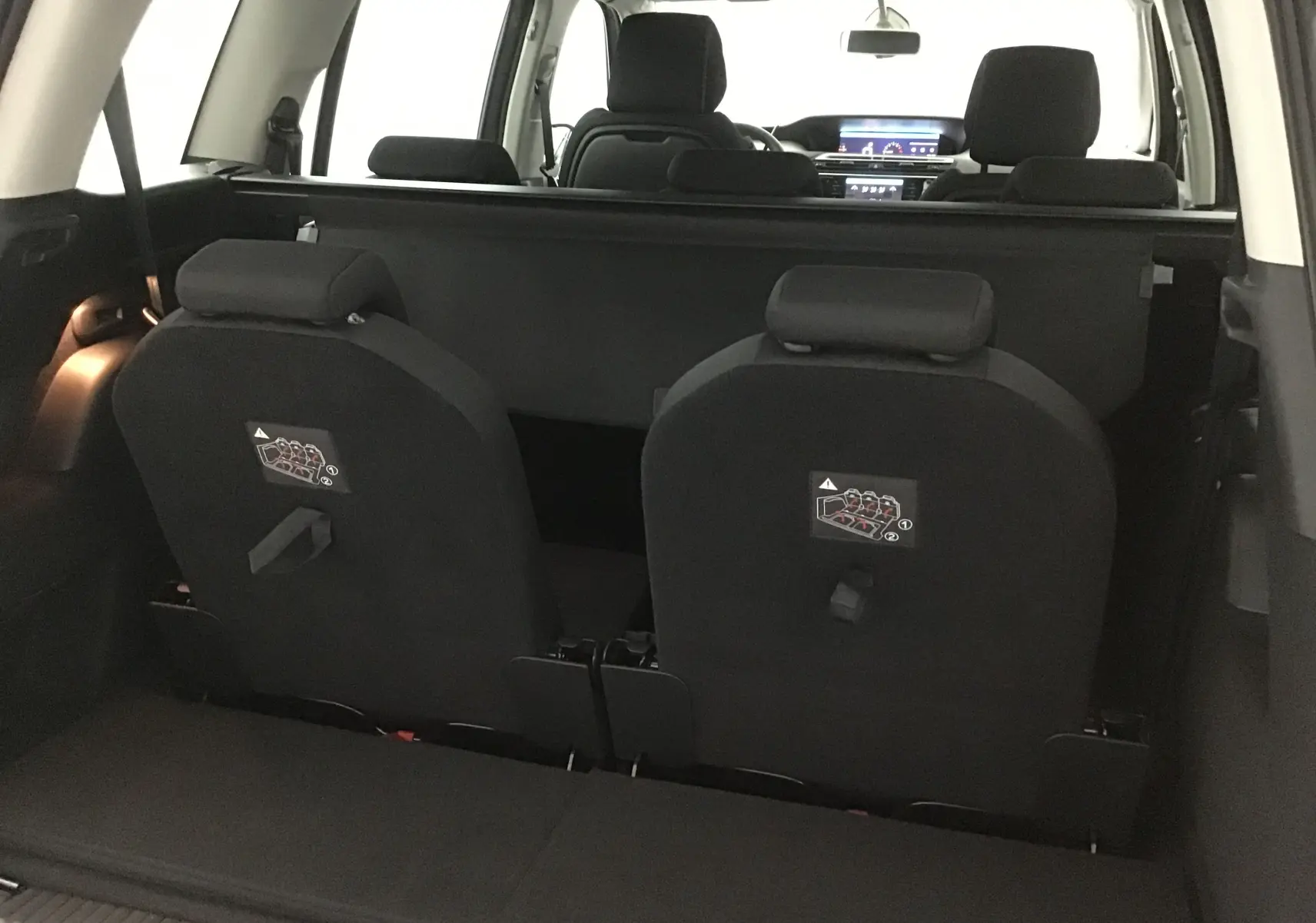 Vue intérieure arrière du Citroën Grand C4 Spacetourer gris, montrant les sièges rabattus et l'habitacle avant lumineux.
