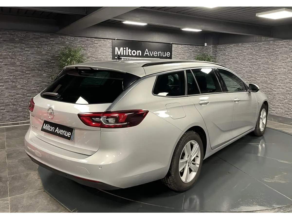 Vue 3/4 arrière droite d'une Opel Insignia Sports Tourer gris métallisé avec vitres arrière surteintées en intérieur showroom.