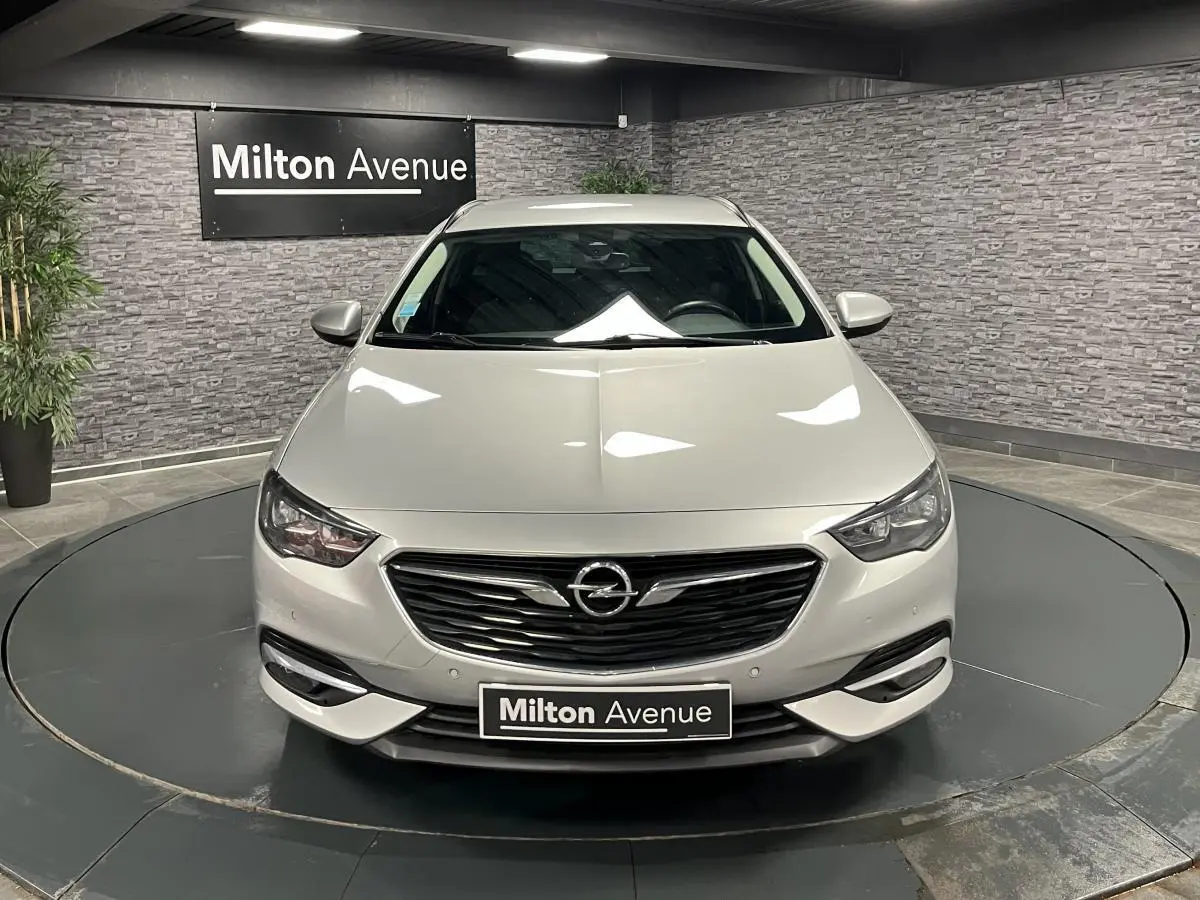 Opel Insignia Sports Tourer gris métallisé vue de face dans un showroom avec calandre noire et phares LED.