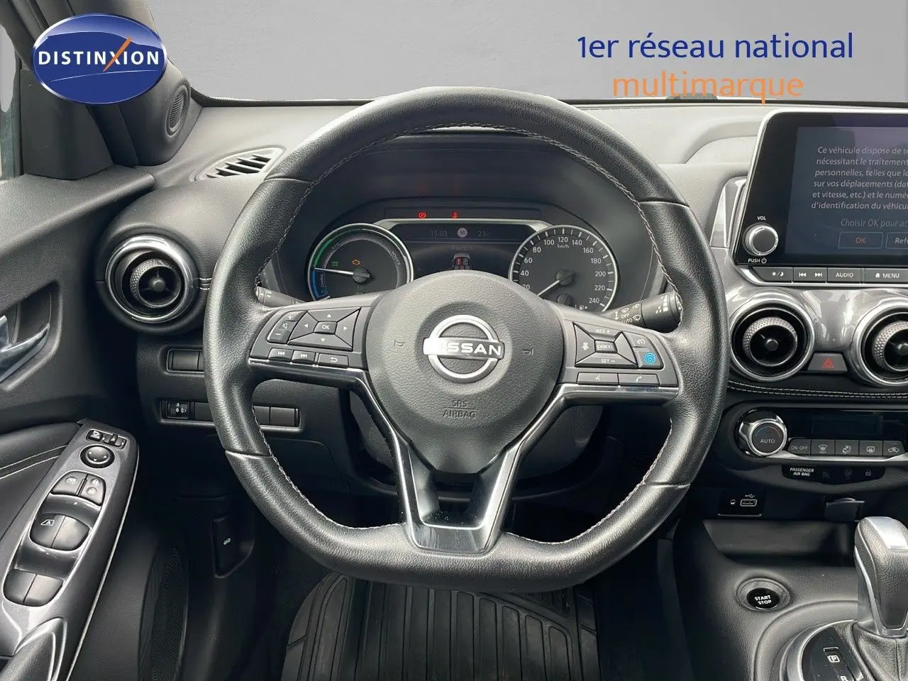 Vue intérieure centrée sur le volant cuir noir du Nissan Juke Hybrid 2023 avec tableau de bord et écran tactile visibles.