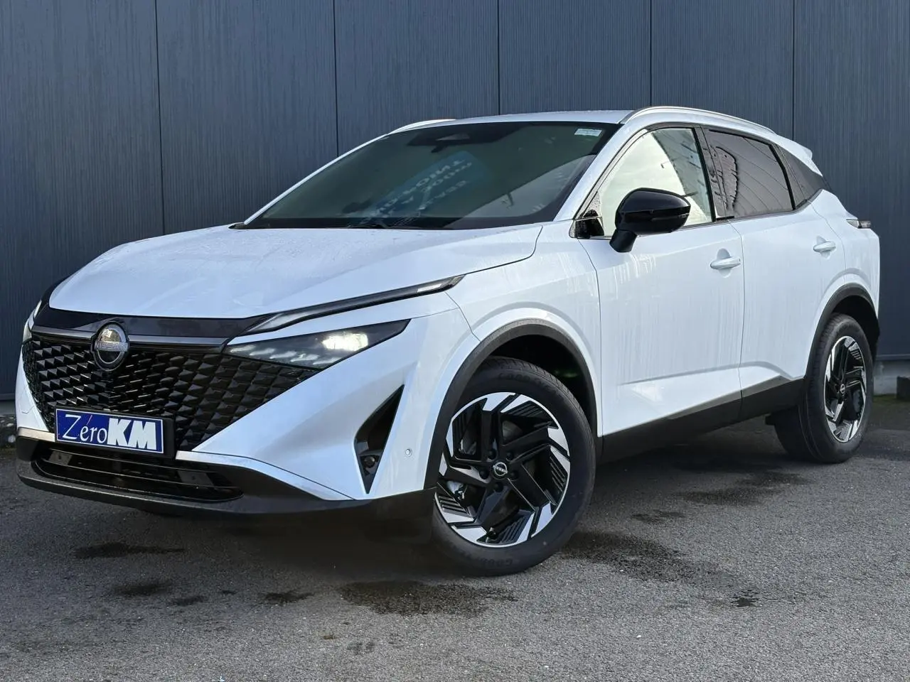 Nissan Qashqai blanc nacré en 3/4 avant droit, avec calandre noire et jantes alliage bicolores distinctives.