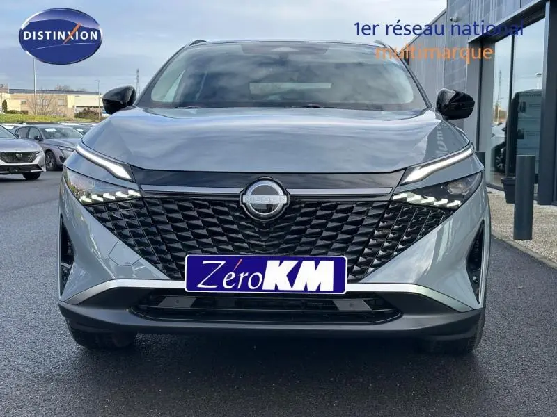 Vue frontale du Nissan Qashqai Hybrid e-POWER 2025 en gris Argile, avec calandre noire et feux LED distinctifs allumés.