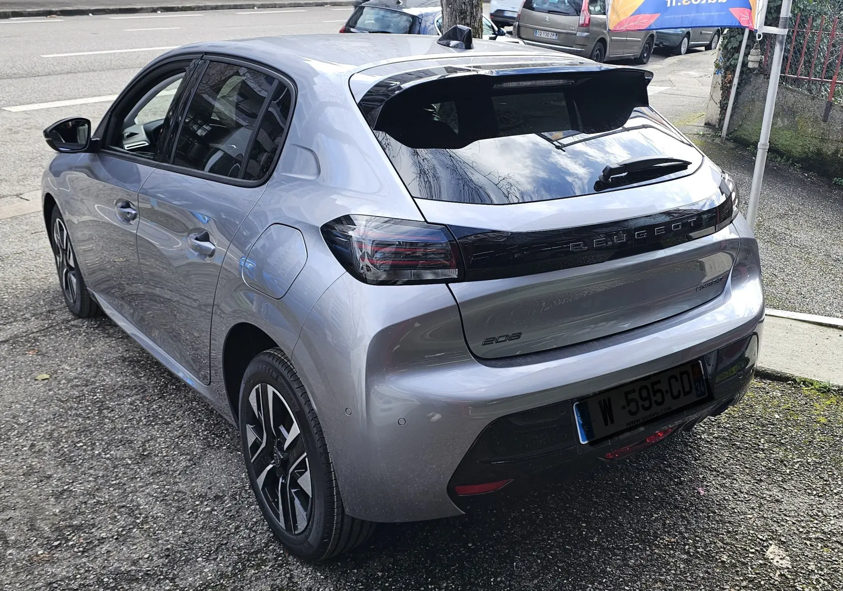 PEUGEOT 208 hybride grise vue 3/4 arrière droit, avec hayon noir brillant et feux arrière fumés.