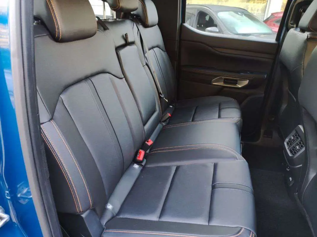 Vue intérieure côté gauche des sièges arrière en cuir noir avec surpiqûres orange du Ford Ranger 2025 bleu lightning.