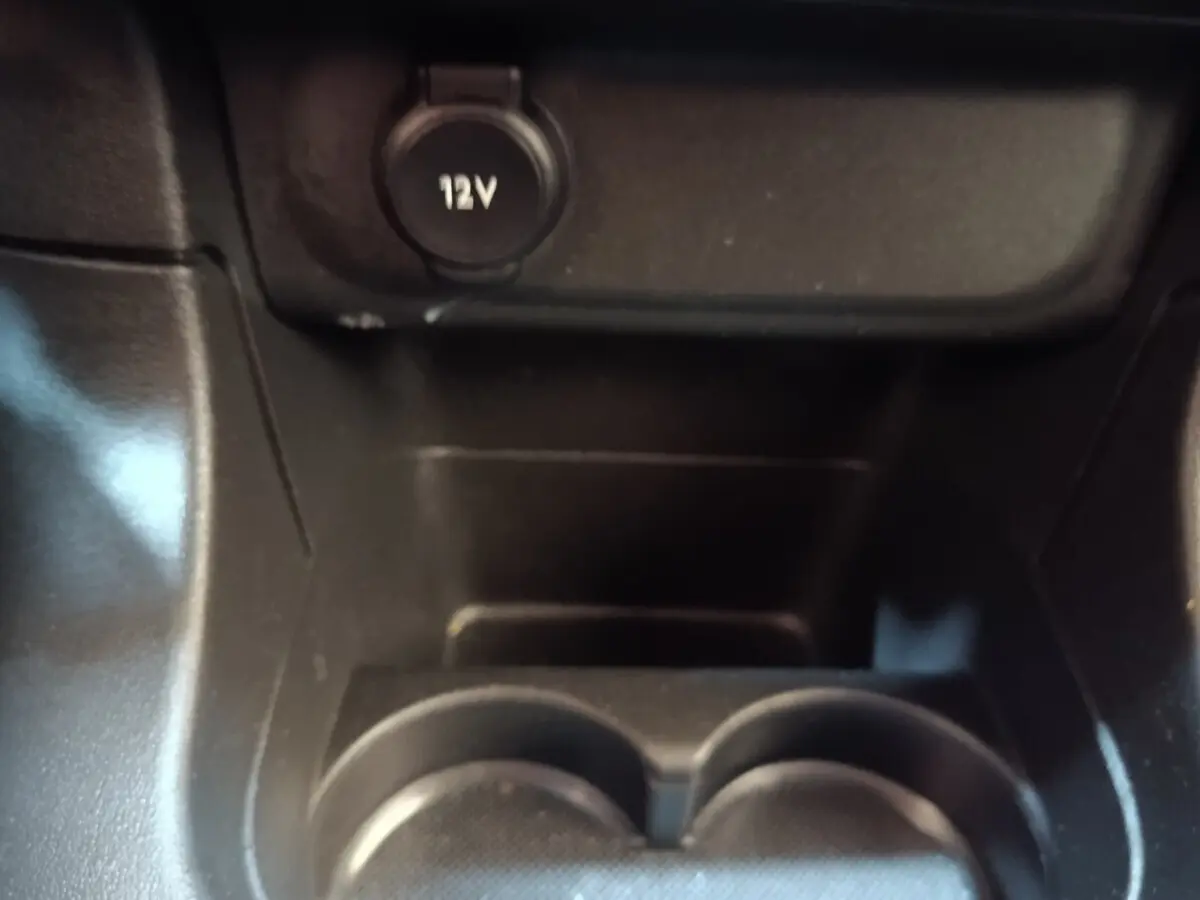 Gros plan sur la prise 12V et porte-gobelets noirs dans l'habitacle d'une Citroën C3 blanche.