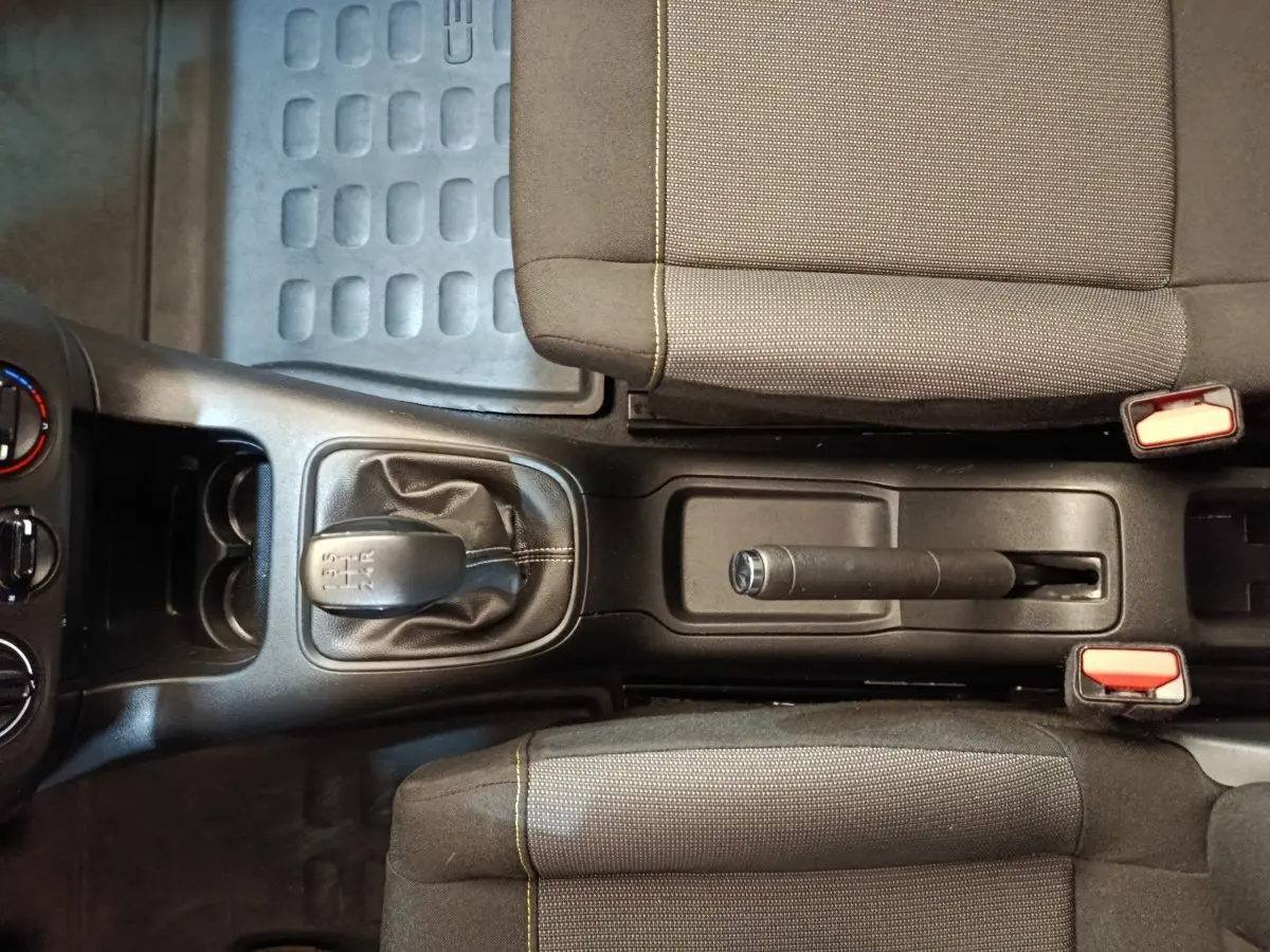 Vue de dessus de la console centrale noire avec levier de vitesse manuel et frein à main entre deux sièges tissu gris du Citroën C3 blanc.