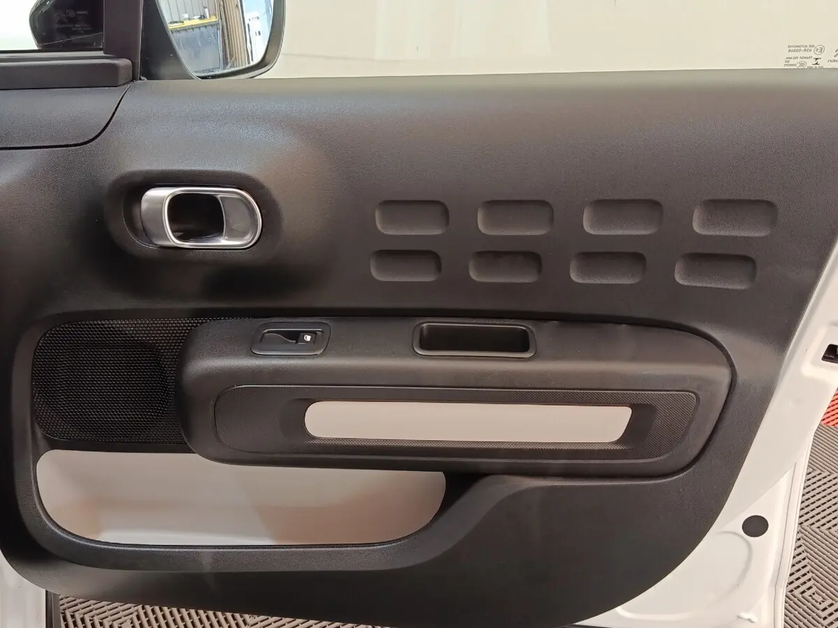 Vue intérieure de la porte avant gauche d'une Citroën C3 blanche, avec poignée chromée et panneau noir texturé.