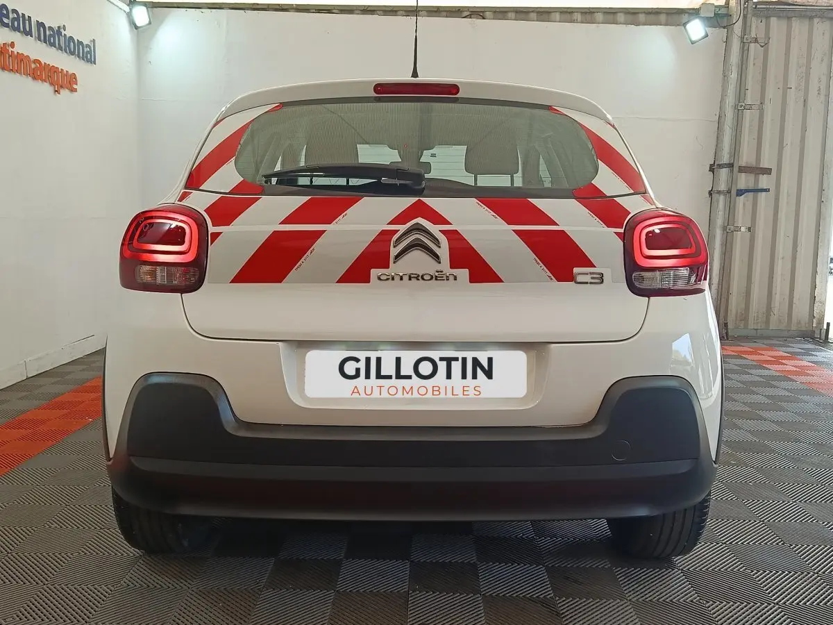 Vue arrière d'une Citroën C3 blanche 2021 avec marquages rouges en chevrons et feux arrière allumés en intérieur.