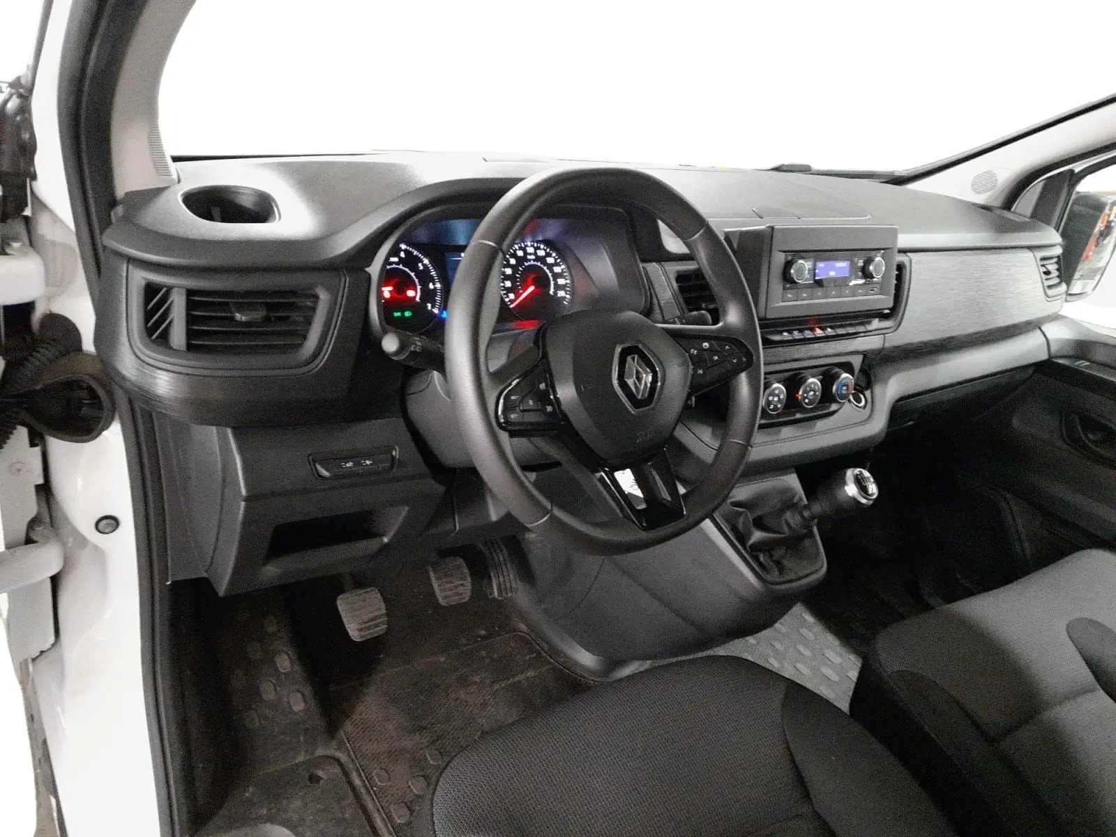 Vue intérieure côté conducteur du Renault Trafic Fourgon blanc, montrant le tableau de bord, volant et levier de vitesses manuel.