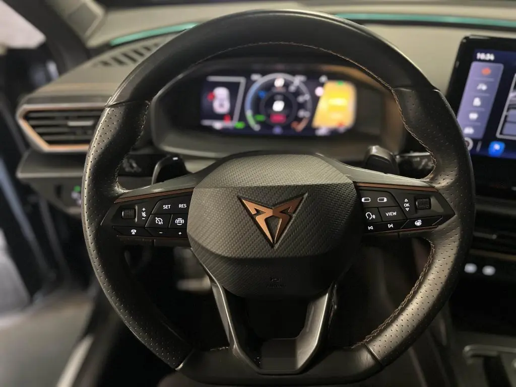 Gros plan sur le volant sport en cuir noir avec logo cuivre du CUPRA Formentor 1.4 e-Hybrid 2023, tableau de bord digital en arrière-plan.