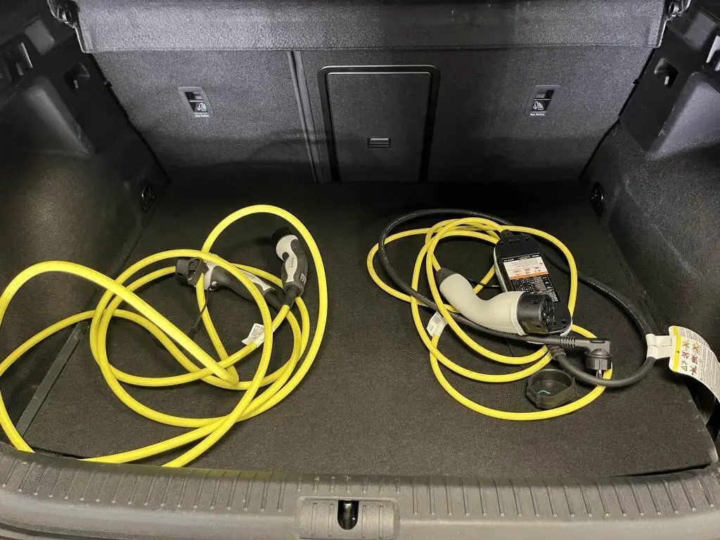 Coffre ouvert d'une CUPRA Formentor gris avec câbles de recharge jaune pour hybride rechargeable visibles.