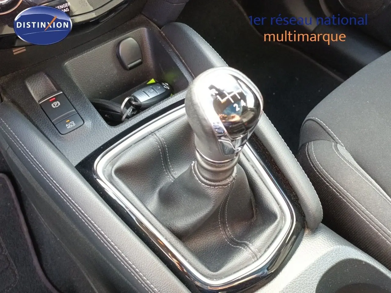 Gros plan sur le levier de vitesse manuel chromé et cuir noir du Nissan Qashqai blanc, intérieur tissu noir.