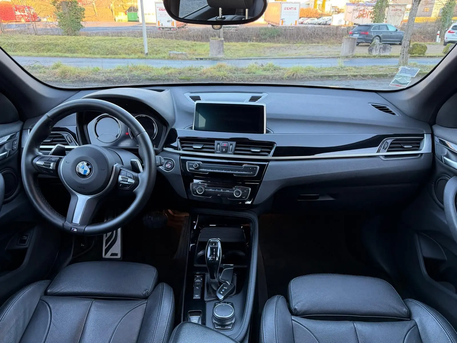 Vue intérieure frontale du tableau de bord et volant noir cuir du BMW X1 18D M Sport, avec écran central et console brillante.