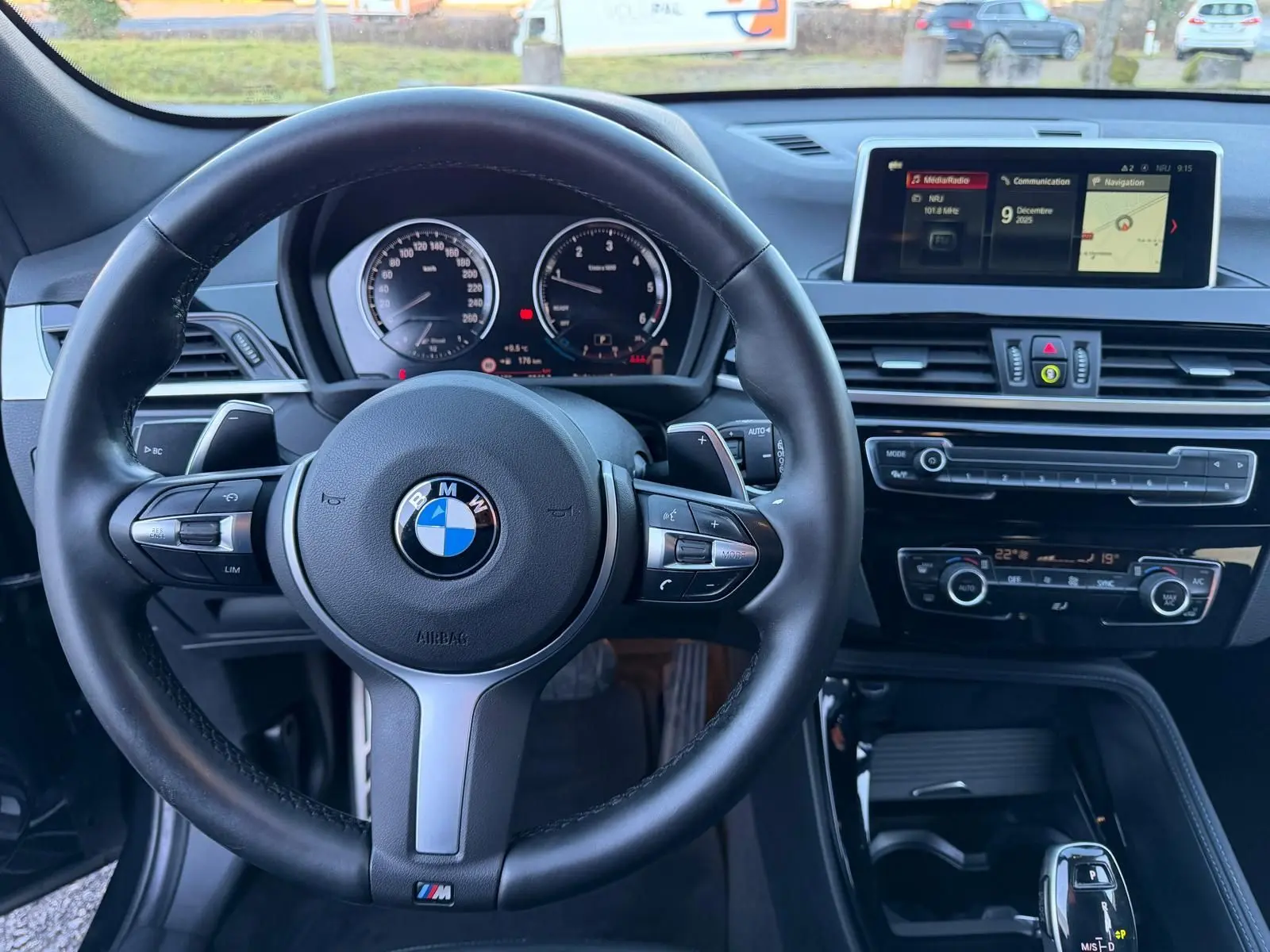 Vue intérieure centrée sur le volant cuir noir et le tableau de bord avec écran multimédia du BMW X1 noir métal 2018 M Sport.