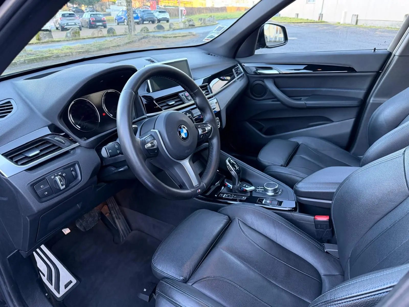 Vue intérieure côté conducteur du BMW X1 18D M Sport 2018, avec volant cuir, tableau de bord moderne et sièges en cuir noir Dakota.