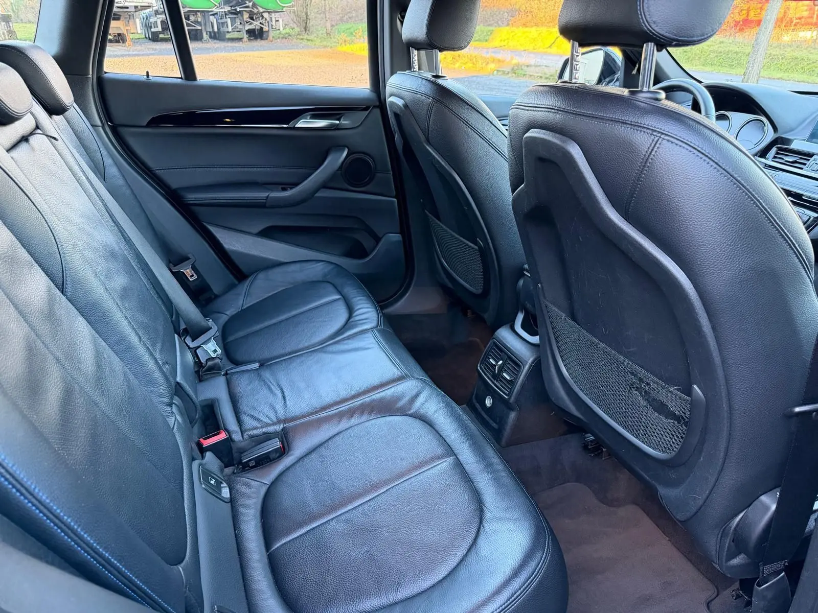 Vue intérieure arrière du BMW X1 18D 2018, montrant les sièges en cuir noir perforé et les dossiers des sièges avant.