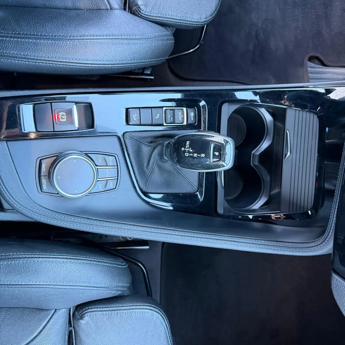 Vue plongeante sur la console centrale noire brillante du BMW X1 18D M Sport 2018 avec levier de vitesse automatique et sièges cuir noir.