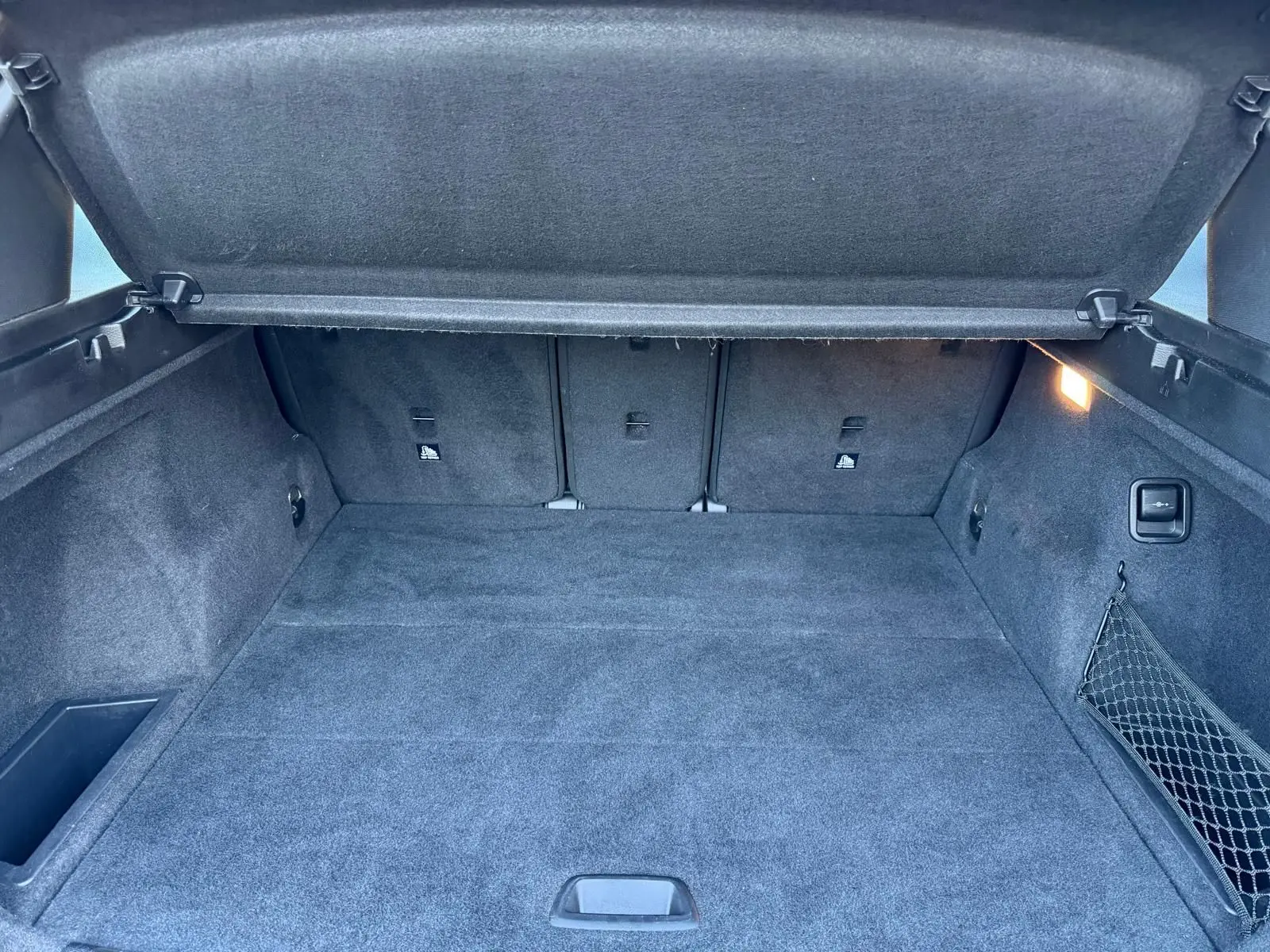 Vue intérieure du coffre spacieux et propre du BMW X1 18D noir métal, avec cache-bagages relevé et éclairage latéral allumé.