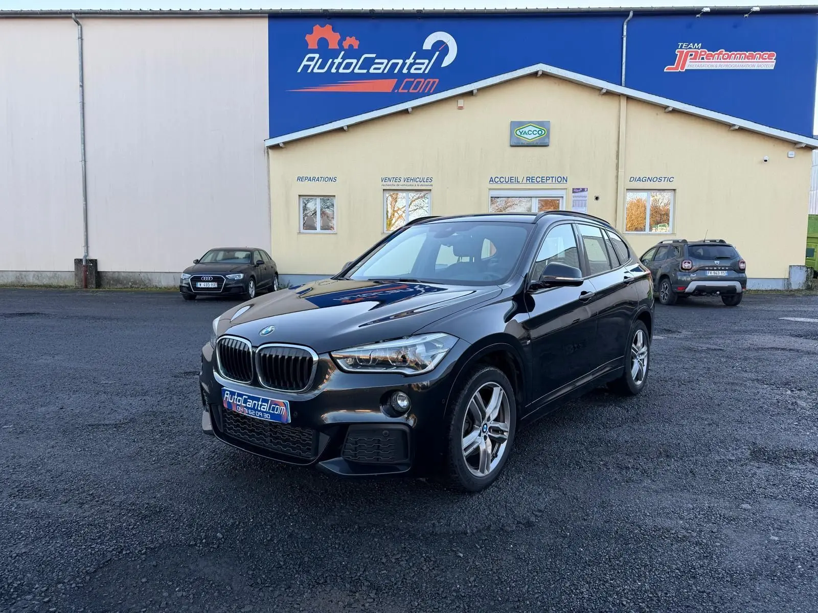 BMW X1 18D noir métal en 3/4 avant droit, finition M Sport avec calandre et jantes distinctives visibles.