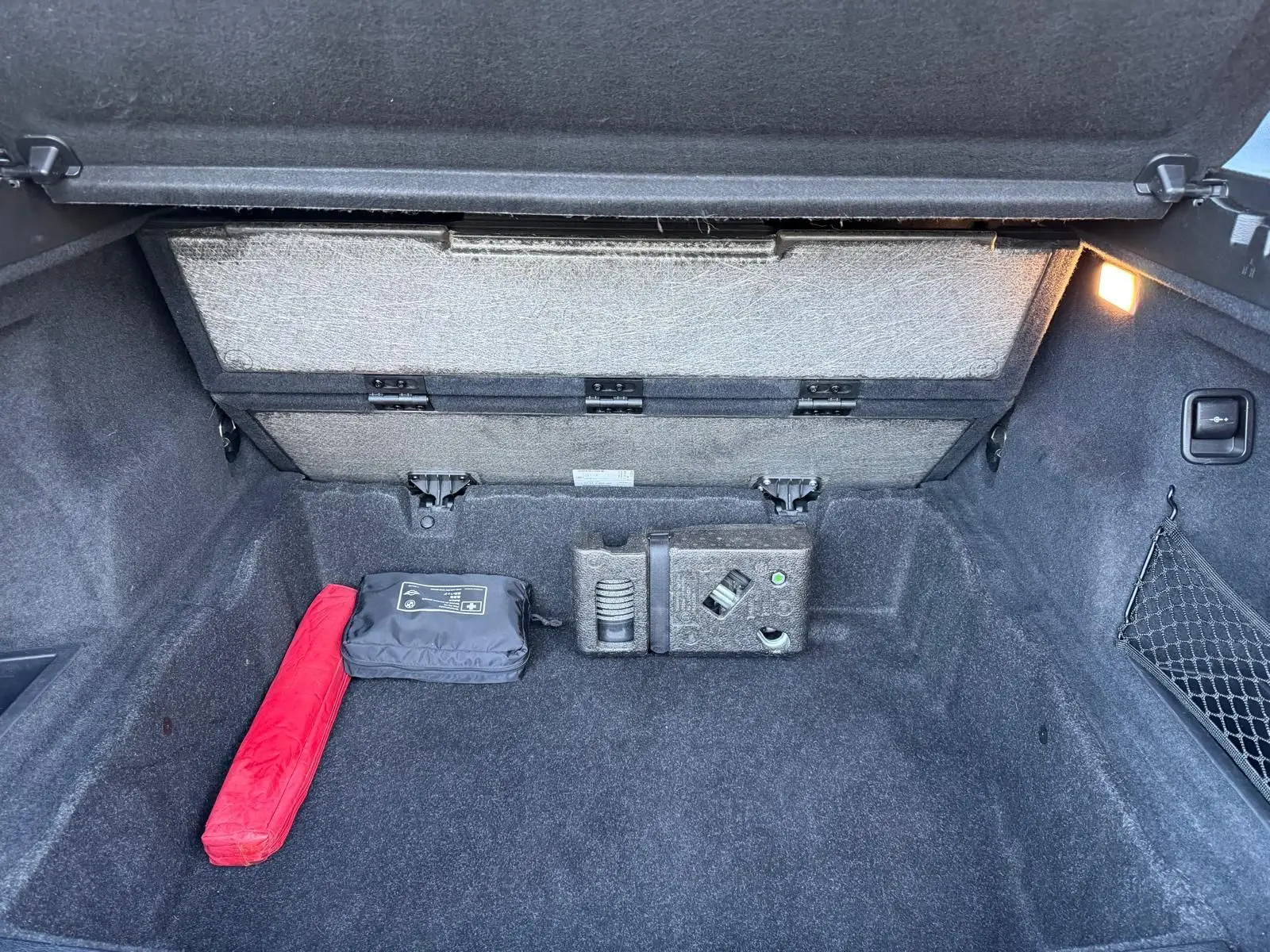 Coffre ouvert d'un BMW X1 noir métal 2018, montrant un espace de rangement avec trousse de secours et filet latéral.