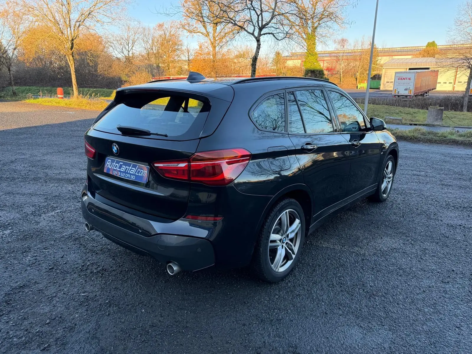 BMW X1 18D noir métal en vue 3/4 arrière droit, avec jantes alliage et double sortie d'échappement visible.