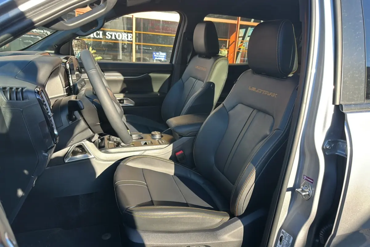 Vue intérieure côté conducteur du Ford Ranger Wildtrak 2025 gris iconic, sièges cuir noirs avec surpiqûres orange.