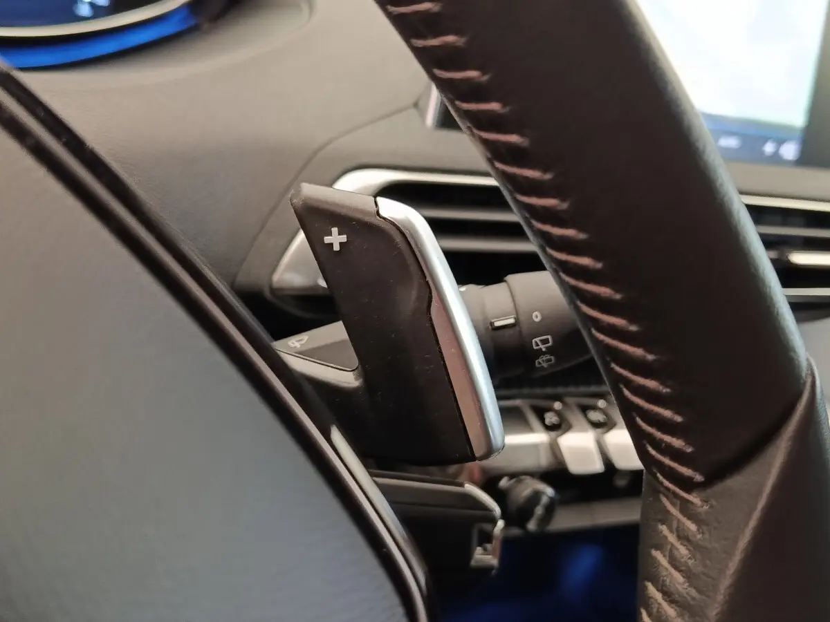 Gros plan sur la palette de changement de vitesse + au volant cuir du Peugeot 5008 gris foncé, intérieur moderne.