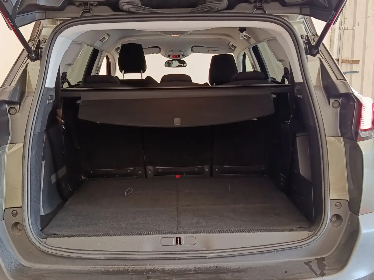 Vue arrière du coffre ouvert d'un Peugeot 5008 gris foncé, avec cache-bagages et sièges arrière visibles.
