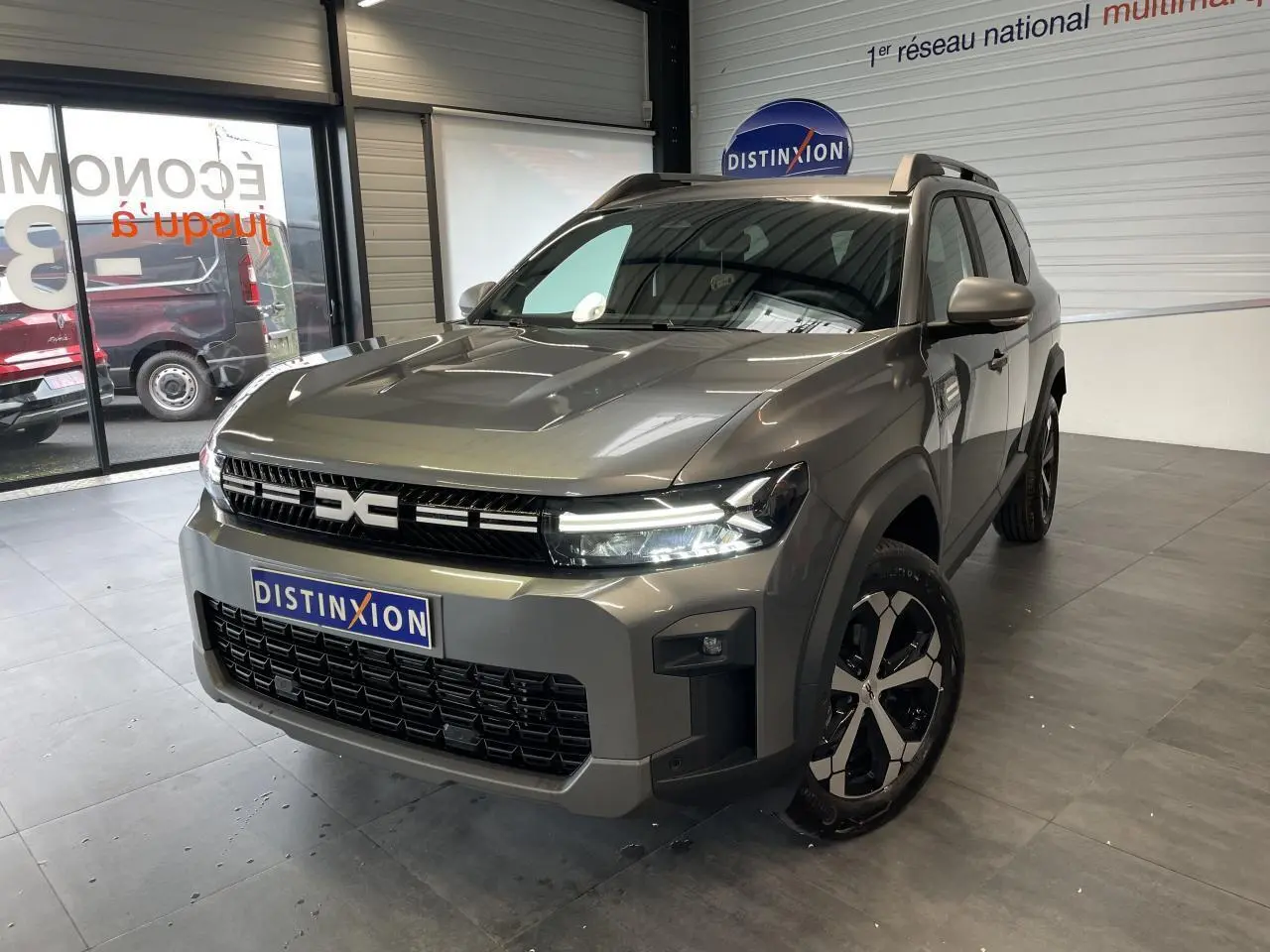 Vue 3/4 avant du Dacia Bigster gris schiste avec calandre noire et jantes alliage bicolores dans un showroom.